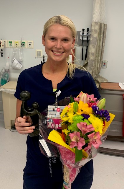 Danynn Dugas in nursing scrubs holding award plaque and trophy