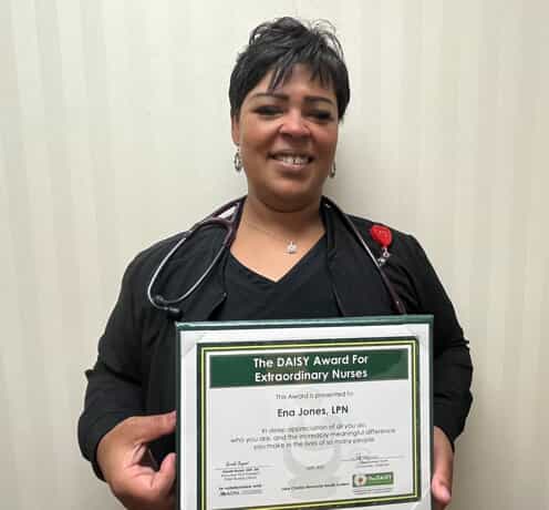 Ena Jones in nursing scrubs holding award plaque and trophy