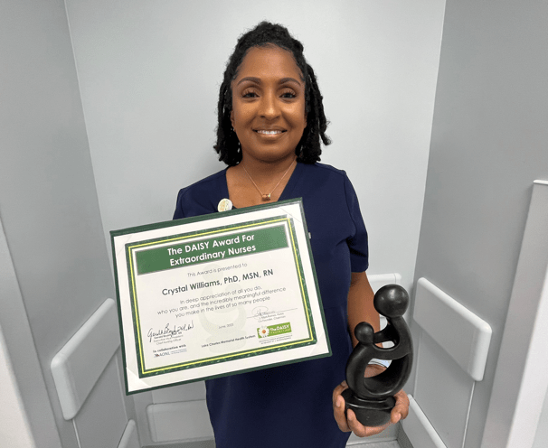 Crystal Williams in nursing scrubs holding award plaque and trophy