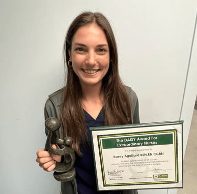 Kasey Aguillard in nursing scrubs holding award plaque and trophy